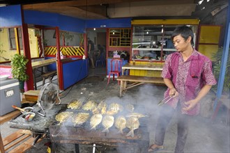 Javanese man grilling fish in a restaurant