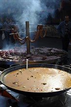 Large pan containing broth in front of giant barbecue at the annual All Saints Market in Cocentaina