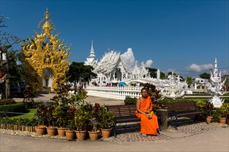 Monk sitting in front of the ornate golden entrance of Wat Rong Khun