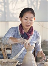Woman molding a piece of pottery on a wheel head
