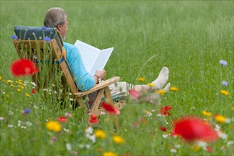 Elderly man readding in a garden chair on a flower meadow