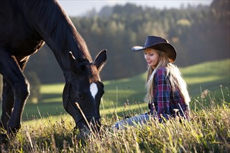 A young woman with a black Hanoverian horse on a mountain meadow in autumn