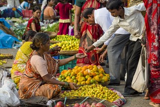 A woman is selling oranges and other fruits at the weekly vegetable market
