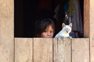Girl and a cat looking out the window of a wooden hut