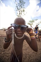 Himba child wearing traditional clothes and sunglasses in a typical village near Kamanjab
