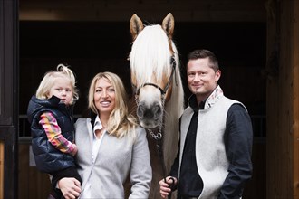 Young family standing with a Tyrolean Haflinger in front of a stall