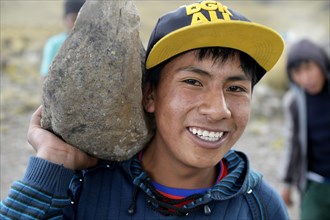 Young man carrying a heavy stone to secure the shores of an artificial lake for irrigation