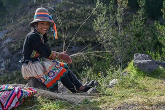 Indio girl with hat smiles and weaves Pacha grass