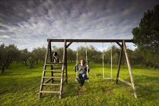 Girl swinging on a wooden swing in front of an olive grove