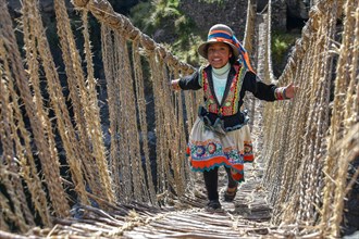 Laughing local girl in traditional costume walks over Inca suspension bridge Q'iswachaka