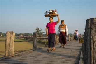 Woman with tanaka on her face carrying food on her head on a teak bridge