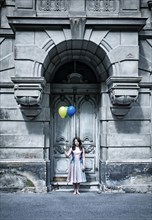 Girl holding balloons in front of an old door