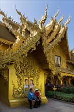 Tourists sitting in front of the gilded toilet house at Wat Rong Khun