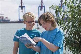 Young people on a language trip reading an English travel guide on the Elbe in front of the Burchard-Kai container terminal