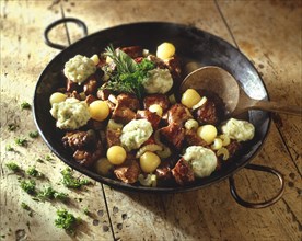 Beef stew and herby dumplings in a black pan on a wood background