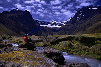 Mountaineer sitting at a mountain stream with the peaks of El Altar or Kapak Urku