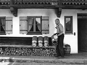 Old man drying milk cans in front of his farm