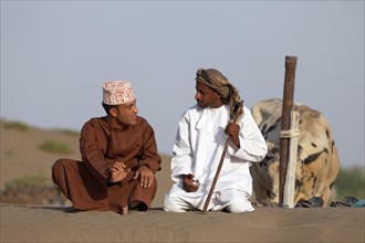 Omanis talking while sitting in traditional clothing