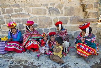 Women and children in traditional dress of the Quechua Indians sitting on the floor in front of a wall
