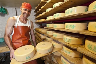 Dairyman with cheese wheels manufactured by him in his cheese cellar
