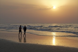 Two men jogging on the beach at sunset