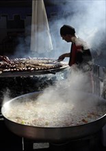 Vegetables boiling in a large pan and man preparing meats on giant barbecue at the annual All Saints Market in Cocentaina