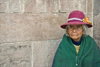 Portrait of an elderly woman in traditional dress of the Quechua Indians sitting on the floor in front of an Inca wall