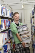 Student carrying a stack of books in the Departmental Library of the University of Hohenheim