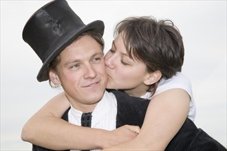 Young man wearing a top hat being tenderly kissed by his partner as he carries her piggyback