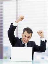 Businessman in an office cheering from behind a laptop