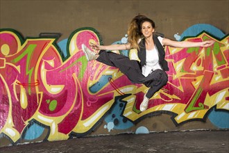 Hip-hop dancer jumping in front of a wall with graffiti
