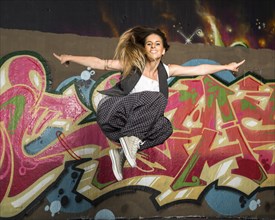 Hip-hop dancer jumping in front of a wall with graffiti