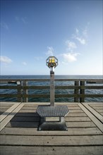 Coin-operated binoculars on a pier in front of the blue sea and blue sky