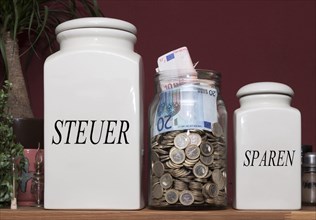 Jar containing money and jars with the signs 'Steuer' and 'Sparen'