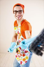 Young man wearing an apron and cleaning gloves holding a broom
