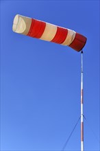 Red and white windsock against a blue sky