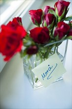 Red roses in vase with a note 'Merci'