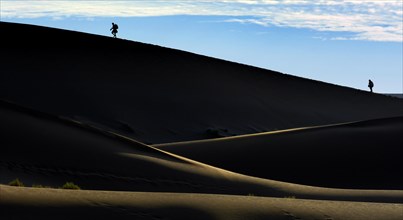 Silhouettes of people climbing a dune