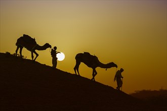 Two Rabari men going down a dune at sunset