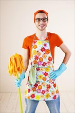 Young man wearing an apron and cleaning gloves holding a cleaning mop