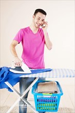 Young man talking on the telephone while doing the ironing