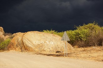 Dark storm front over rocks with signpost 'Epupa 36 km'