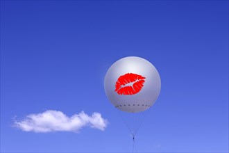 White balloon with printed red lips against a blue sky and a cloud