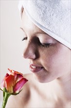 Portrait of a smiling young woman smelling a rose with a towel wrapped around her head
