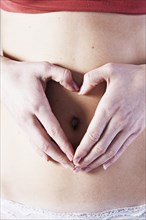 Young woman with her hands forming a heart on her belly