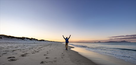 Young man walks on the beach and stretches his arms into the air