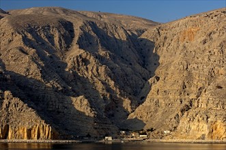 Small village in the morning light at the foot of the rocky cliffs of a fjord in the Musandam Peninsula on the Persian Gulf
