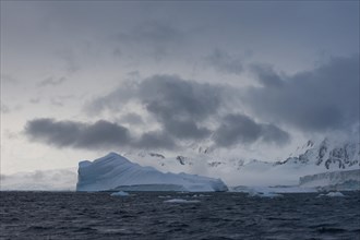 Iceberg in a fjord with mountain scenery and a cloudy sky
