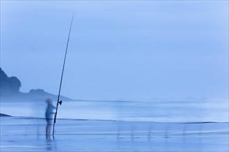 Child on beach with a fishing rod at dusk