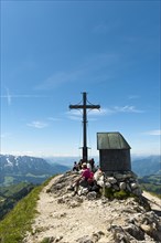 Mountain climber at the summit cross with a small chapel on Geigelstein Mountain